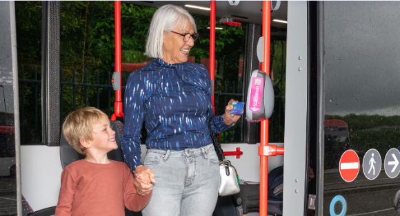 Oudere mevrouw met kleine jongen aan haar hand betaald met betaalpas in de bus.